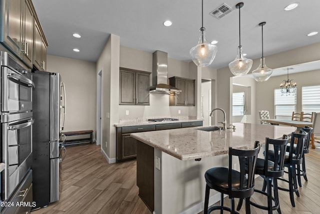 kitchen featuring sink, wood-type flooring, a kitchen island with sink, stainless steel appliances, and wall chimney range hood