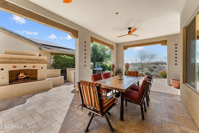 view of patio / terrace with outdoor dining space, a grill, a warm lit fireplace, and ceiling fan