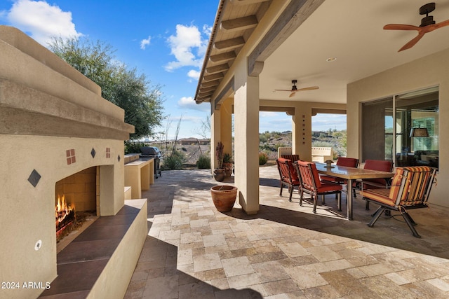 view of patio with grilling area, ceiling fan, a warm lit fireplace, outdoor dining space, and area for grilling