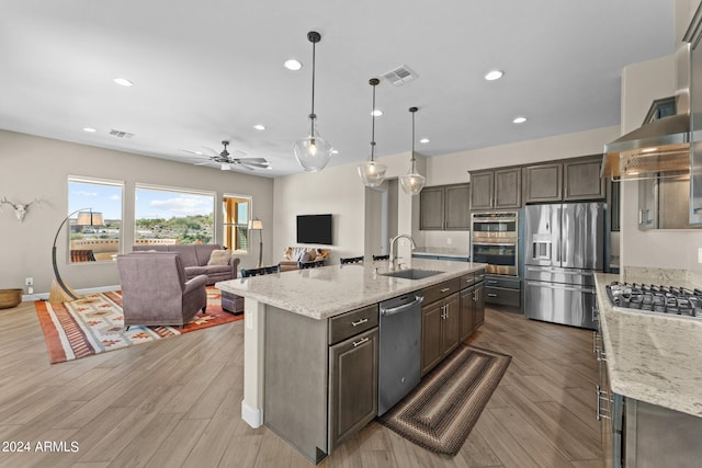 kitchen with light wood-type flooring, appliances with stainless steel finishes, sink, and an island with sink