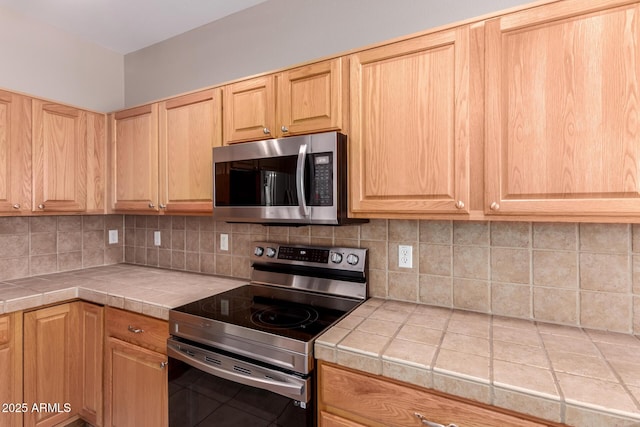 kitchen featuring tile countertops, appliances with stainless steel finishes, backsplash, and light brown cabinets