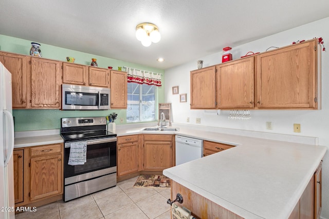 kitchen featuring light tile patterned floors, stainless steel appliances, a peninsula, a sink, and light countertops