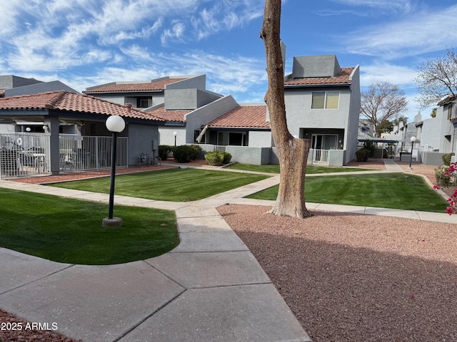 rear view of property with fence, a yard, a tiled roof, a residential view, and stucco siding