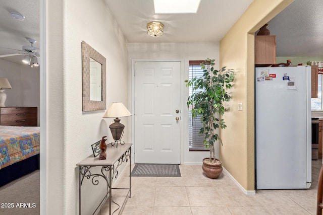 tiled entryway with a skylight, ceiling fan, and baseboards