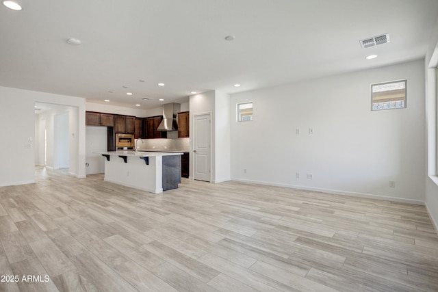 4515 Charro Ct, Wickenburg, AZ 85390 - kitchen featuring wall chimney range hood, open floor plan, a kitchen bar, light wood-type flooring, and recessed lighting