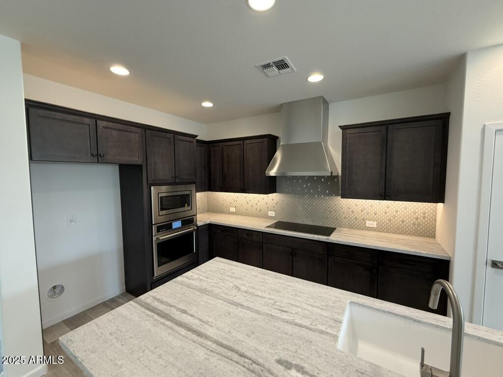 4515 Charro Ct, Wickenburg, AZ 85390 - kitchen featuring appliances with stainless steel finishes, wall chimney range hood, a sink, light wood-type flooring, and tasteful backsplash
