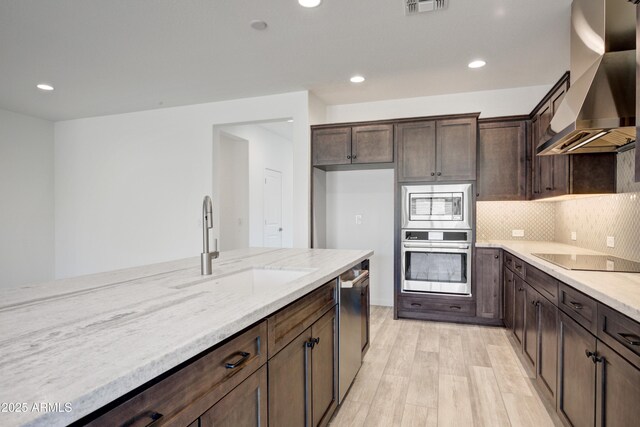 4515 Charro Ct, Wickenburg, AZ 85390 - kitchen featuring stainless steel appliances, wall chimney range hood, light wood-style floors, light stone counters, and dark brown cabinetry