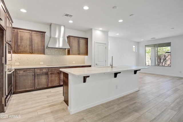 4515 Charro Ct, Wickenburg, AZ 85390 - kitchen with wall chimney exhaust hood, a kitchen bar, a kitchen island with sink, light stone countertops, and a sink
