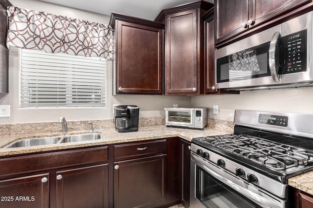 kitchen with dark brown cabinetry, a toaster, light stone counters, stainless steel appliances, and a sink