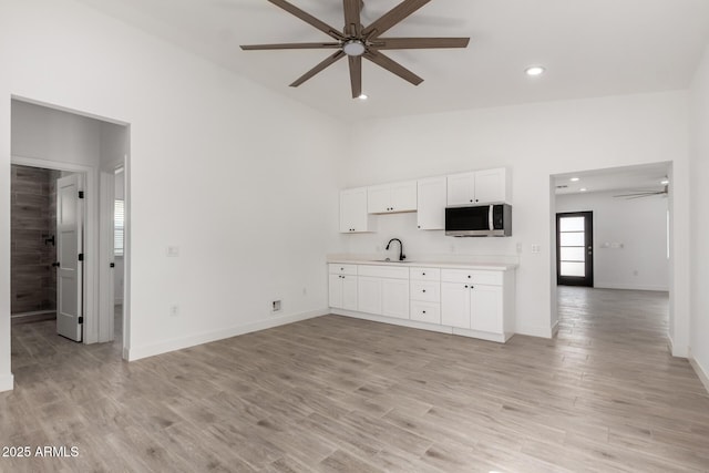kitchen featuring light countertops, white cabinets, ceiling fan, and stainless steel microwave
