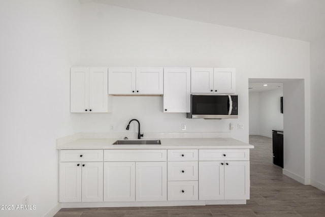 kitchen featuring high vaulted ceiling, a sink, white cabinetry, stainless steel microwave, and baseboards