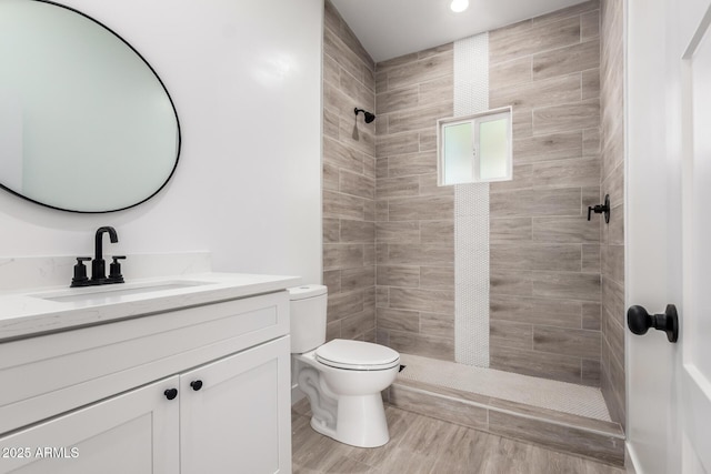 bathroom with toilet, a tile shower, vanity, and recessed lighting