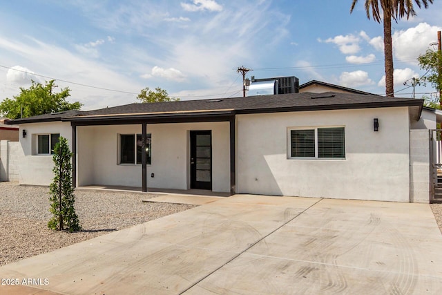 rear view of house with a shingled roof, stucco siding, and a patio area