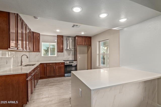 kitchen featuring stainless steel electric range oven, sink, backsplash, kitchen peninsula, and wall chimney range hood