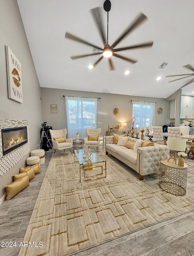 living room with ceiling fan, light hardwood / wood-style floors, and vaulted ceiling