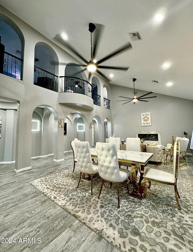 dining area featuring a fireplace, ceiling fan, hardwood / wood-style floors, and high vaulted ceiling