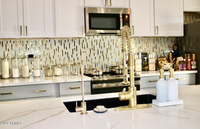 kitchen featuring light stone countertops, appliances with stainless steel finishes, backsplash, and white cabinetry