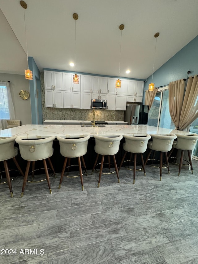 kitchen with light stone countertops, tasteful backsplash, pendant lighting, white cabinets, and appliances with stainless steel finishes