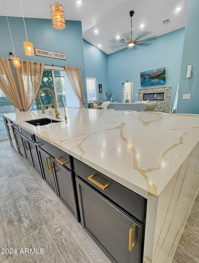 kitchen featuring light stone countertops, ceiling fan, sink, pendant lighting, and a stone fireplace