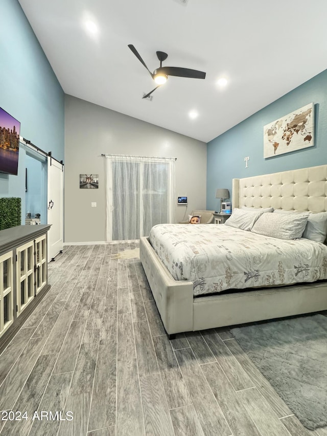 bedroom featuring a barn door, hardwood / wood-style flooring, vaulted ceiling, and ceiling fan