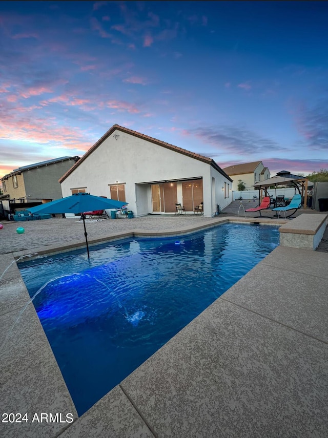 pool at dusk featuring a gazebo, pool water feature, and a patio