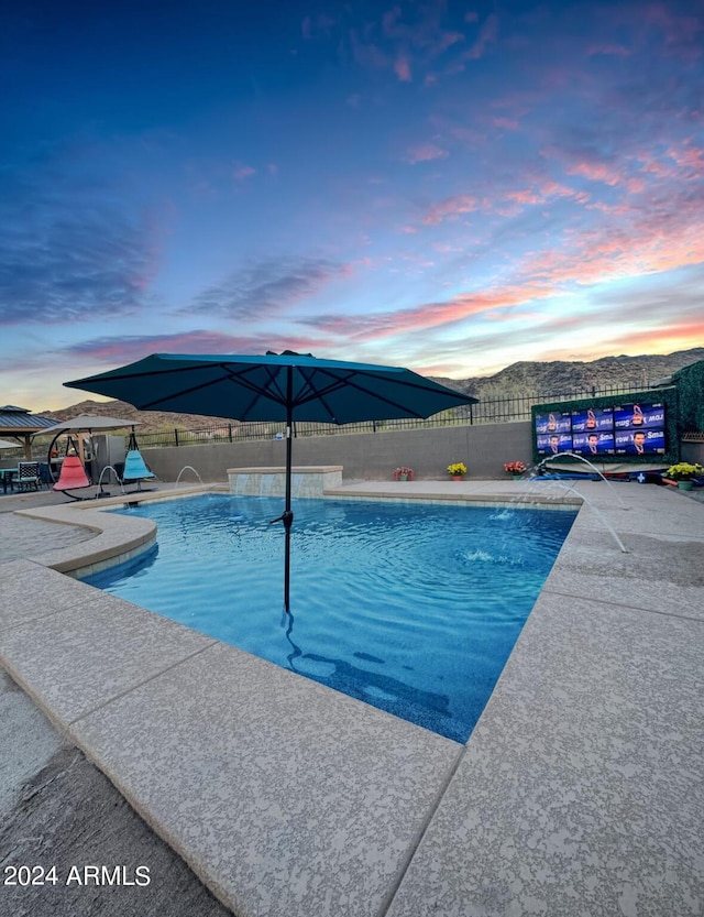 pool at dusk with pool water feature and a patio