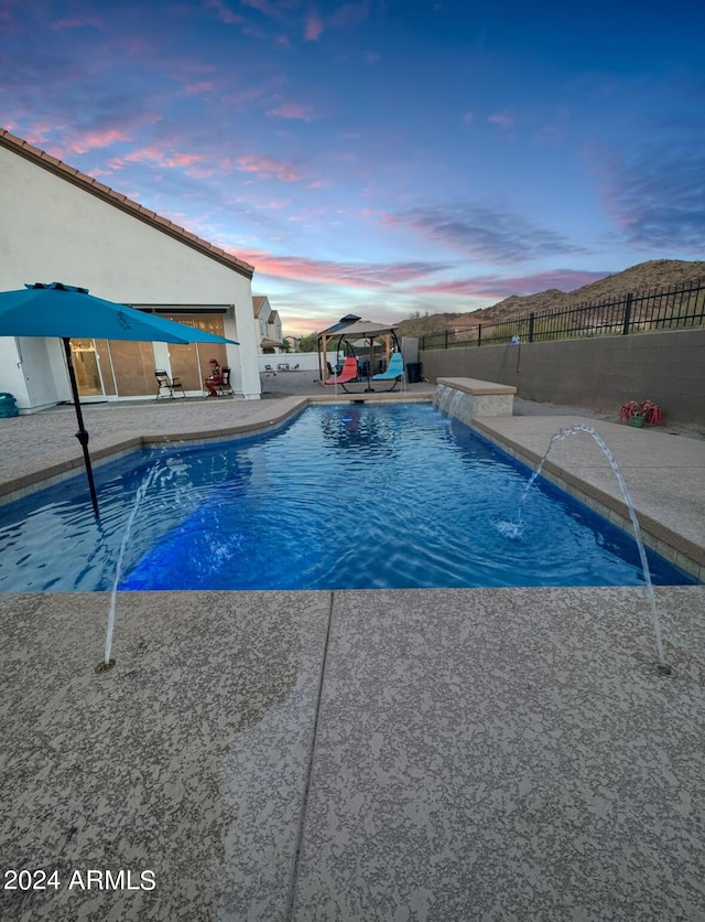 pool at dusk featuring pool water feature and a patio area