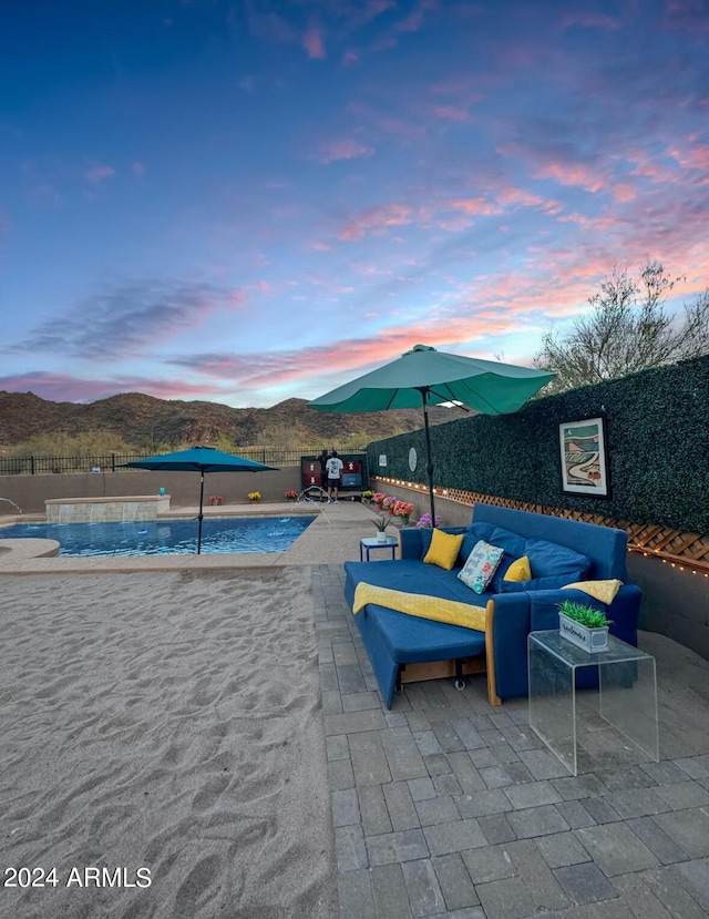 pool at dusk featuring a patio area, a mountain view, and an outdoor living space