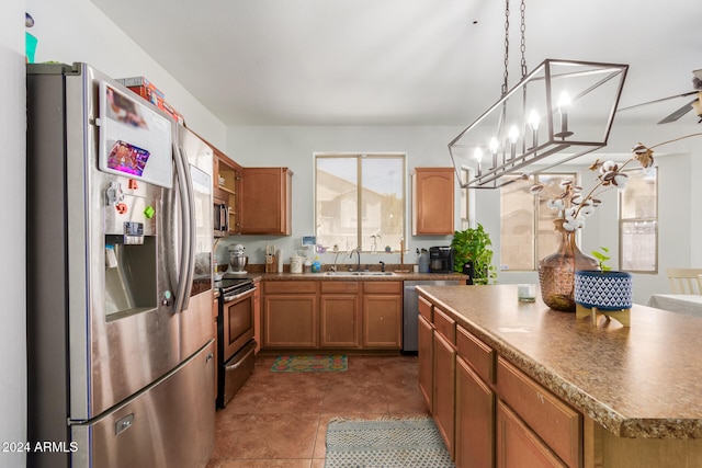 kitchen with ceiling fan with notable chandelier, dark tile patterned flooring, hanging light fixtures, sink, and appliances with stainless steel finishes