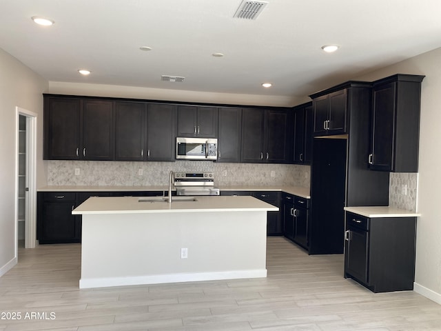 kitchen featuring an island with sink, stainless steel appliances, backsplash, and sink