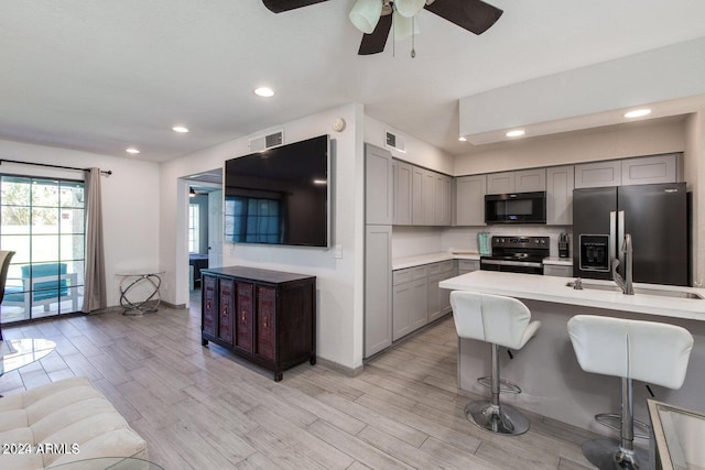 kitchen featuring ceiling fan, light hardwood / wood-style flooring, stainless steel appliances, gray cabinetry, and a breakfast bar area