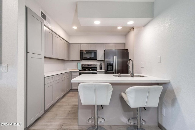 kitchen with gray cabinetry, light hardwood / wood-style flooring, stainless steel appliances, a breakfast bar area, and sink