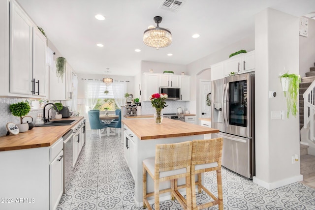 kitchen with wooden counters, stainless steel appliances, a kitchen breakfast bar, white cabinets, and sink