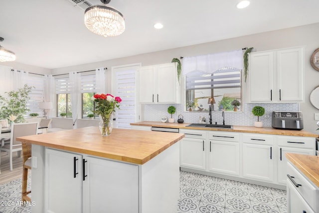 kitchen with butcher block counters, decorative backsplash, sink, white cabinets, and a center island