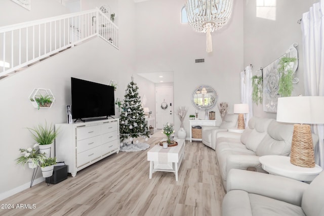 living room featuring plenty of natural light, a towering ceiling, light hardwood / wood-style flooring, and a notable chandelier