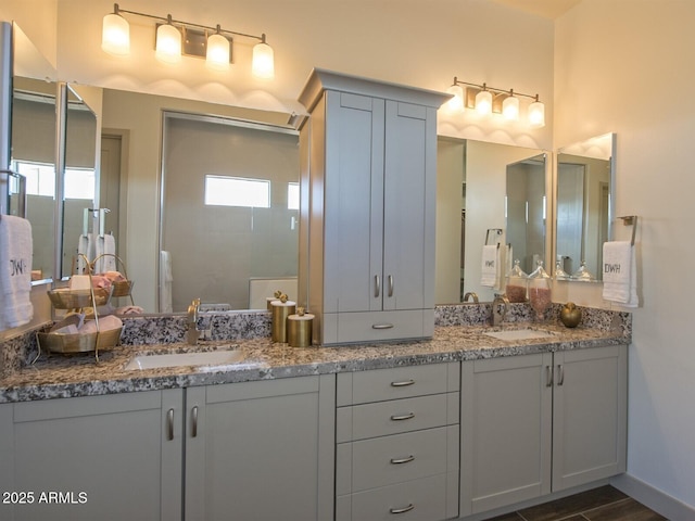 bathroom featuring a walk in shower, double vanity, a sink, and baseboards