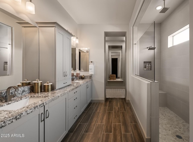 bathroom with double vanity, wood tiled floor, a sink, baseboards, and walk in shower