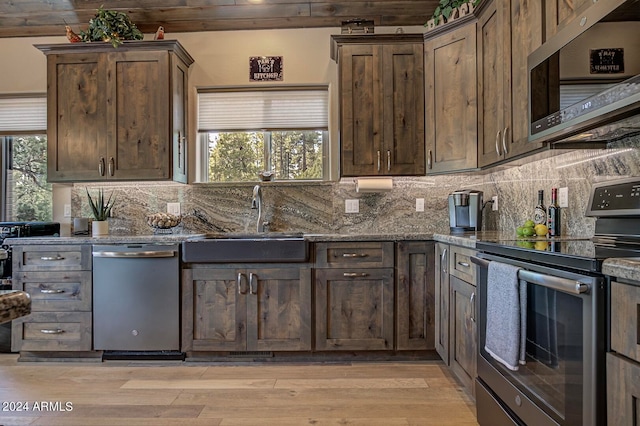 kitchen with stainless steel appliances, light wood-type flooring, dark stone countertops, and backsplash