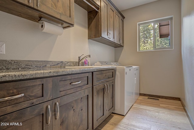 clothes washing area with light hardwood / wood-style flooring, cabinets, washer and dryer, and sink