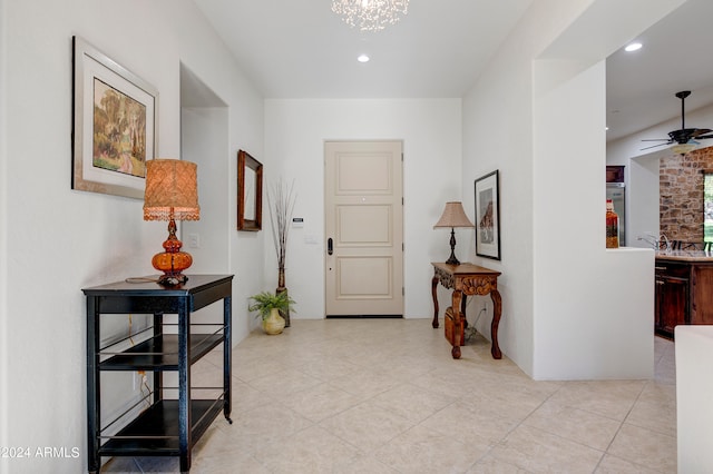 foyer entrance featuring brick wall, light tile flooring, and ceiling fan with notable chandelier