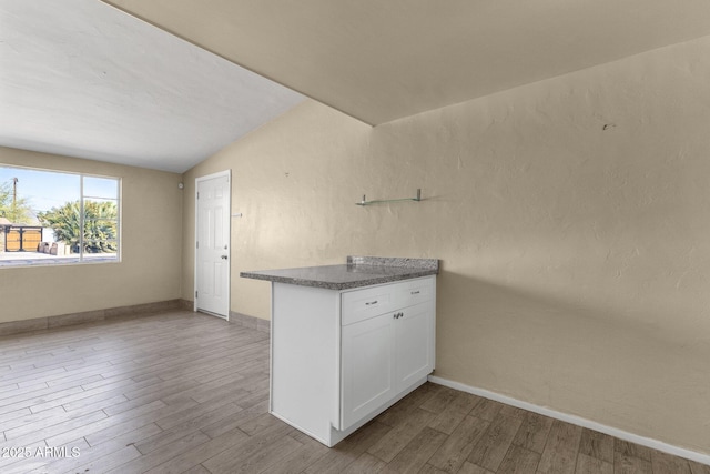 kitchen featuring lofted ceiling, baseboards, white cabinetry, and wood finished floors