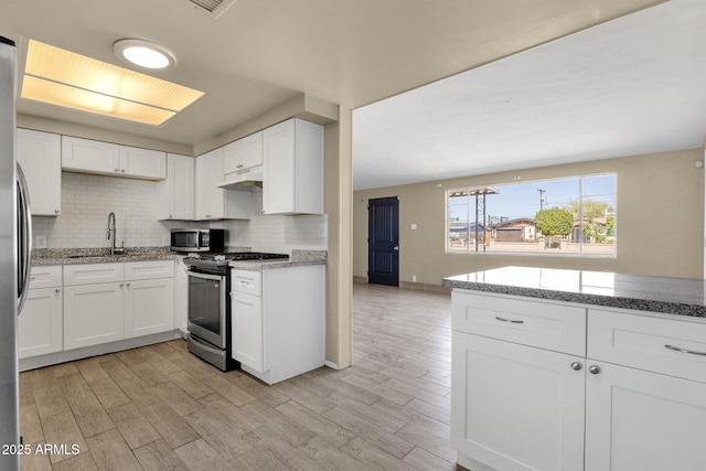 kitchen with tasteful backsplash, appliances with stainless steel finishes, white cabinetry, a sink, and under cabinet range hood