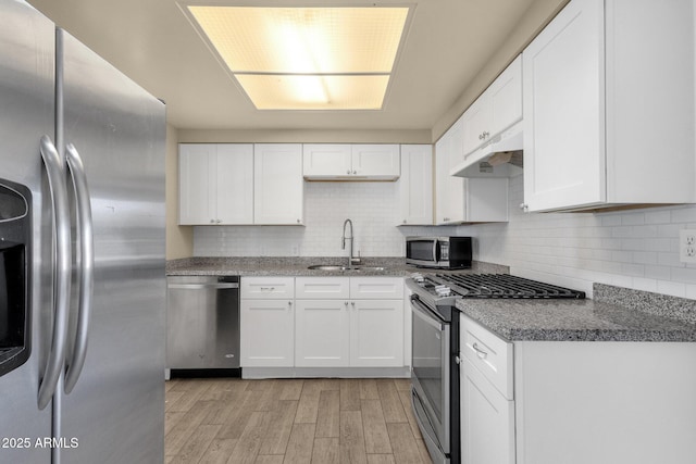 kitchen with decorative backsplash, appliances with stainless steel finishes, under cabinet range hood, white cabinetry, and a sink