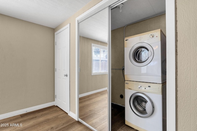 laundry room with laundry area, stacked washer / dryer, wood finished floors, and baseboards