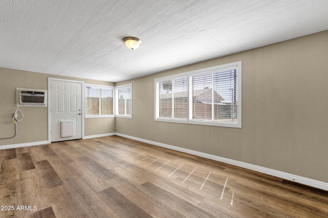 unfurnished room with an AC wall unit, baseboards, and wood finished floors