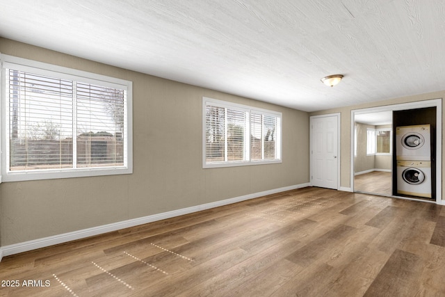 unfurnished bedroom featuring stacked washer / drying machine, multiple windows, baseboards, and wood finished floors