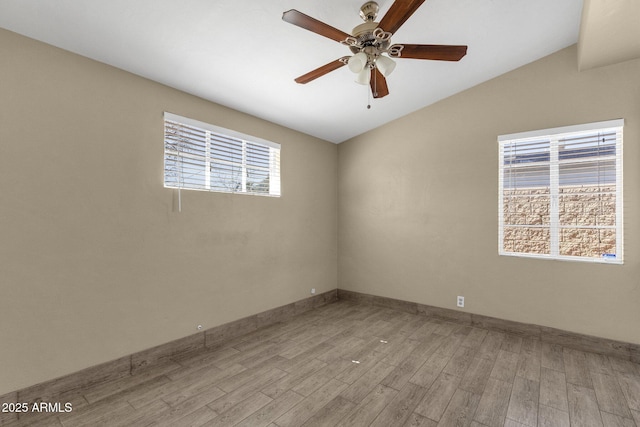 spare room with light wood-style floors, vaulted ceiling, baseboards, and a ceiling fan