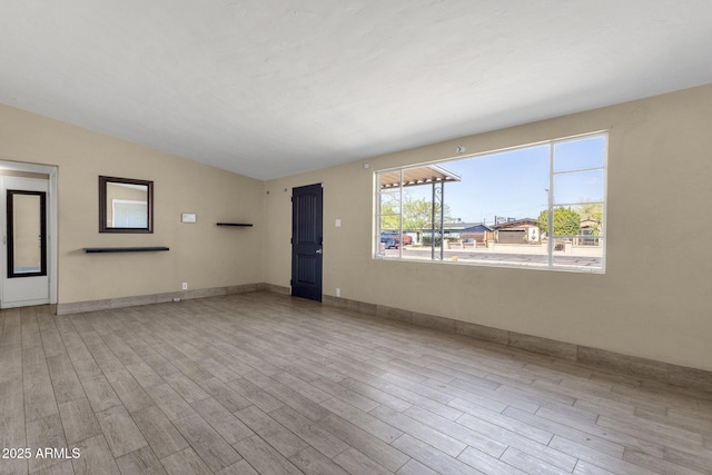 unfurnished living room with lofted ceiling, wood finished floors, and baseboards