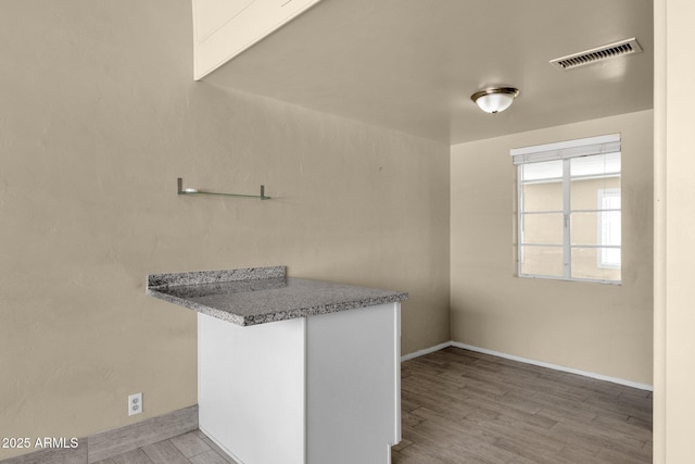 kitchen with baseboards, visible vents, a peninsula, and light wood finished floors