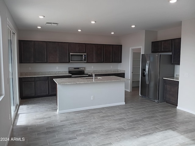 kitchen featuring a center island with sink, sink, light wood-type flooring, appliances with stainless steel finishes, and dark brown cabinetry